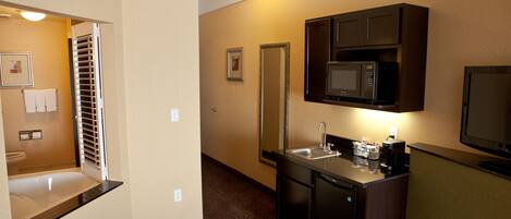 A compact hotel room with a kitchenette, a sink, a microwave, and a large mirror.