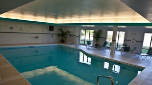 An indoor swimming pool with clear water, a diving board, and lounge chairs.