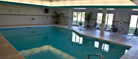An indoor swimming pool with clear water, a diving board, and lounge chairs.
