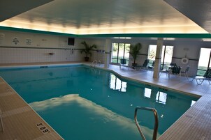 Una piscina interior con agua cristalina, un trampolín y sillas de descanso.