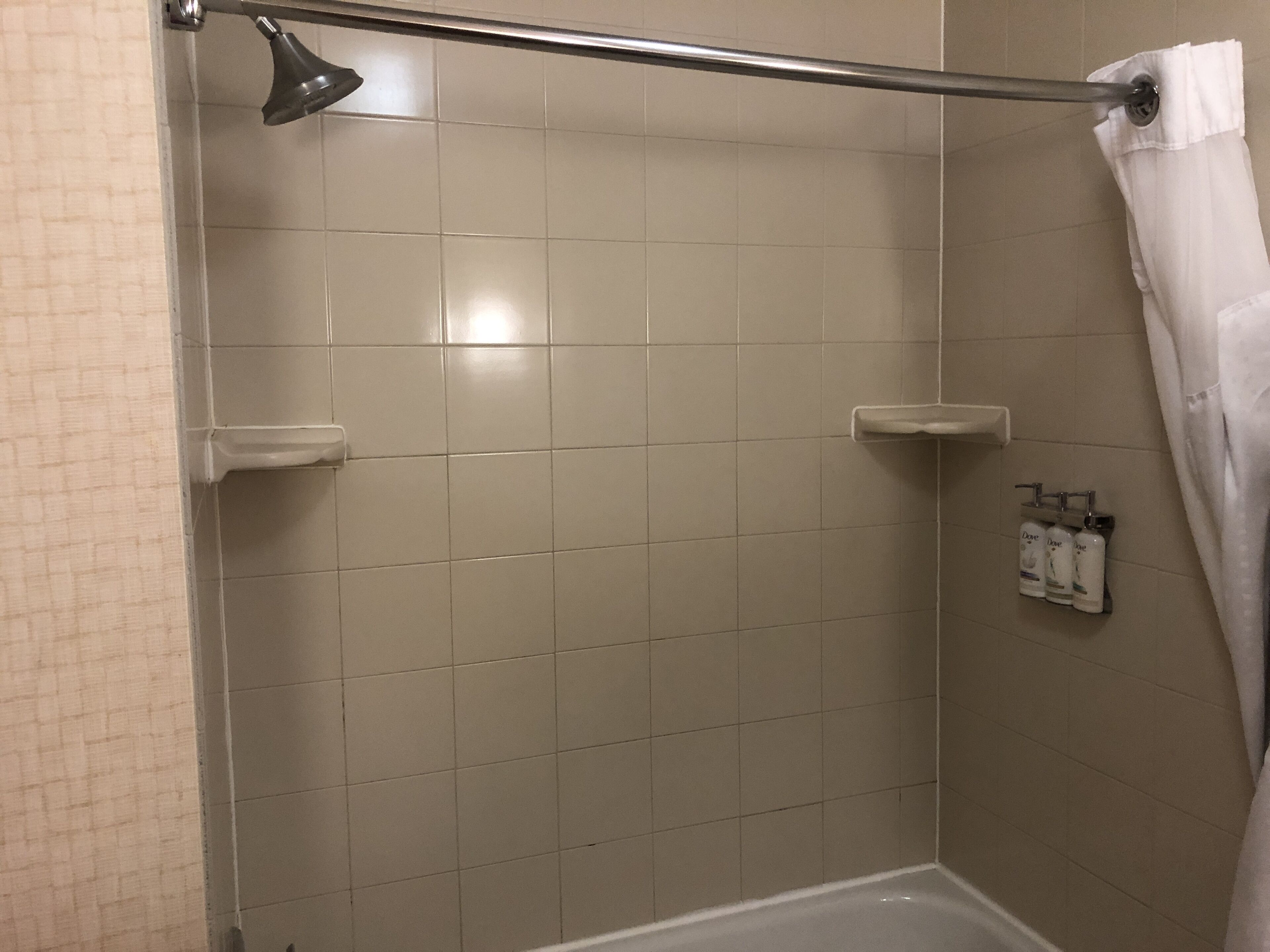A shower with a handheld showerhead, a towel rack with a towel, and toiletries on a wall-mounted shelf.