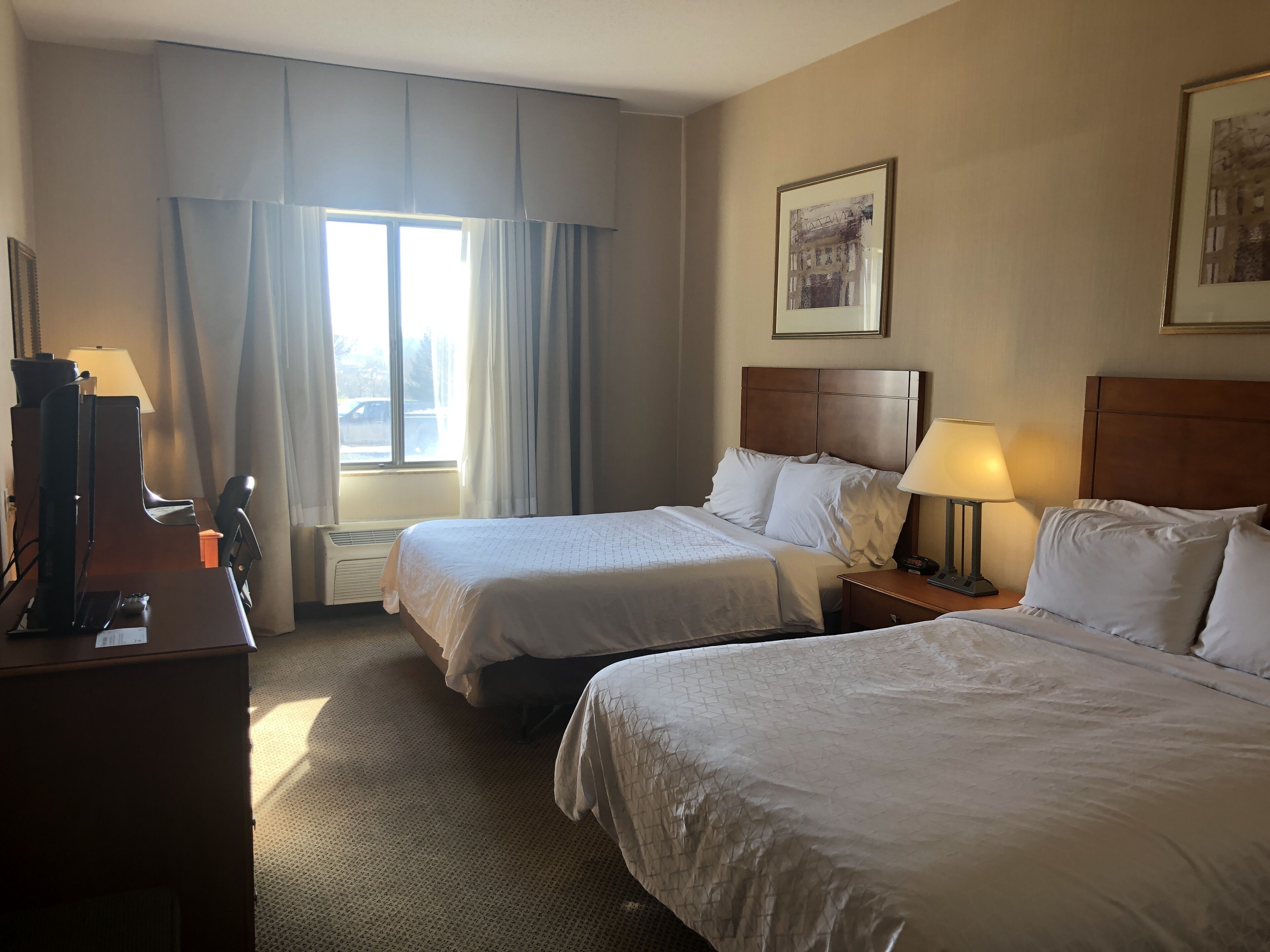 Een hotelkamer met twee bedden, een bureau met een computer, een stoel en een raam met gordijnen.