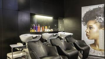 A modern salon with black leather chairs, white sinks, and a large mirror.