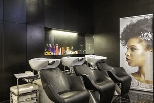 A modern salon with black leather chairs, white sinks, and a large mirror.