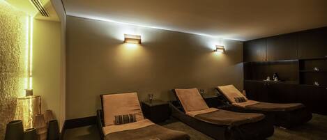 A spa room with two massage beds, a wall-mounted heater, and a dark wooden cabinet.