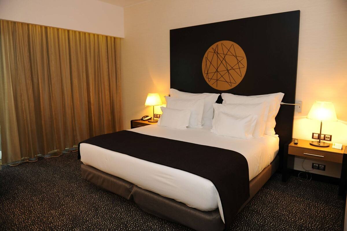 A hotel room with a large bed, two bedside tables with lamps, a headboard with a geometric design, and a curtain.