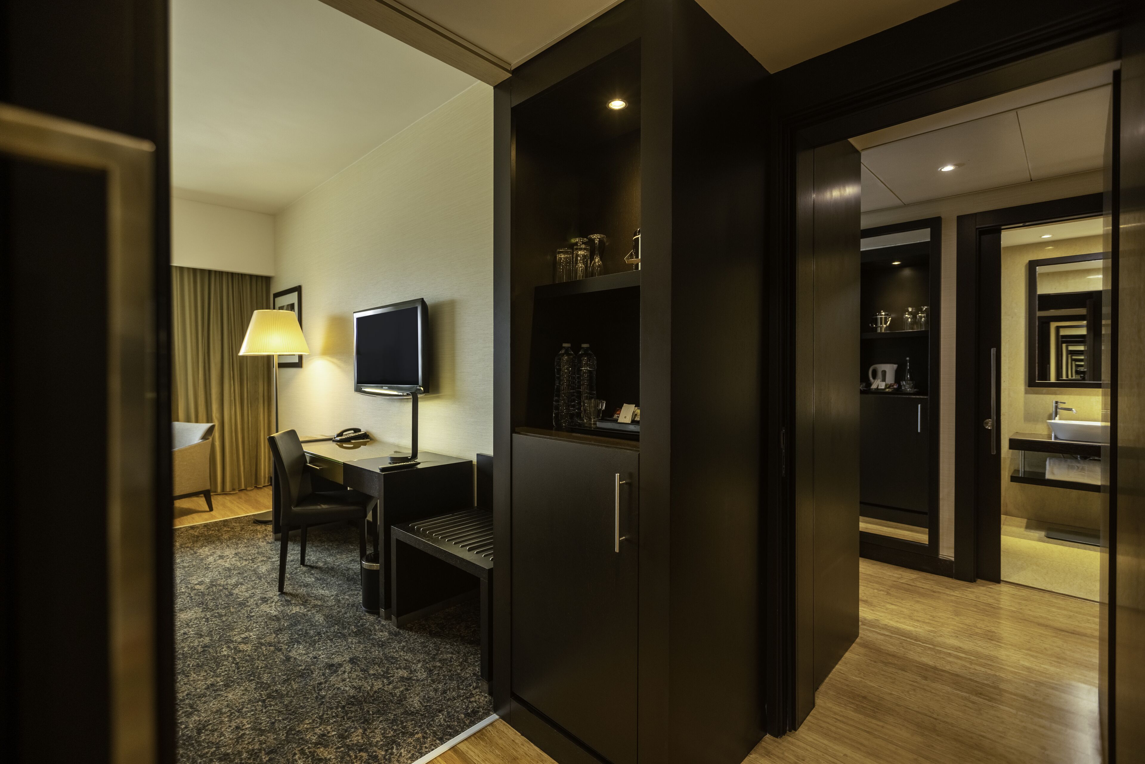 A hotel room with a desk, chair, TV, wardrobe, and a bathroom visible through an open door.