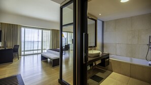 A modern hotel room with a large bed, a sitting area, a desk, and a bathroom with a bathtub and sink. - EPIC SANA Luanda Hotel (Luanda)