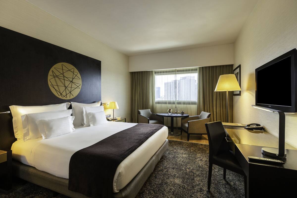 A hotel room with a large bed, a desk with a chair, a TV, and a window with curtains.
