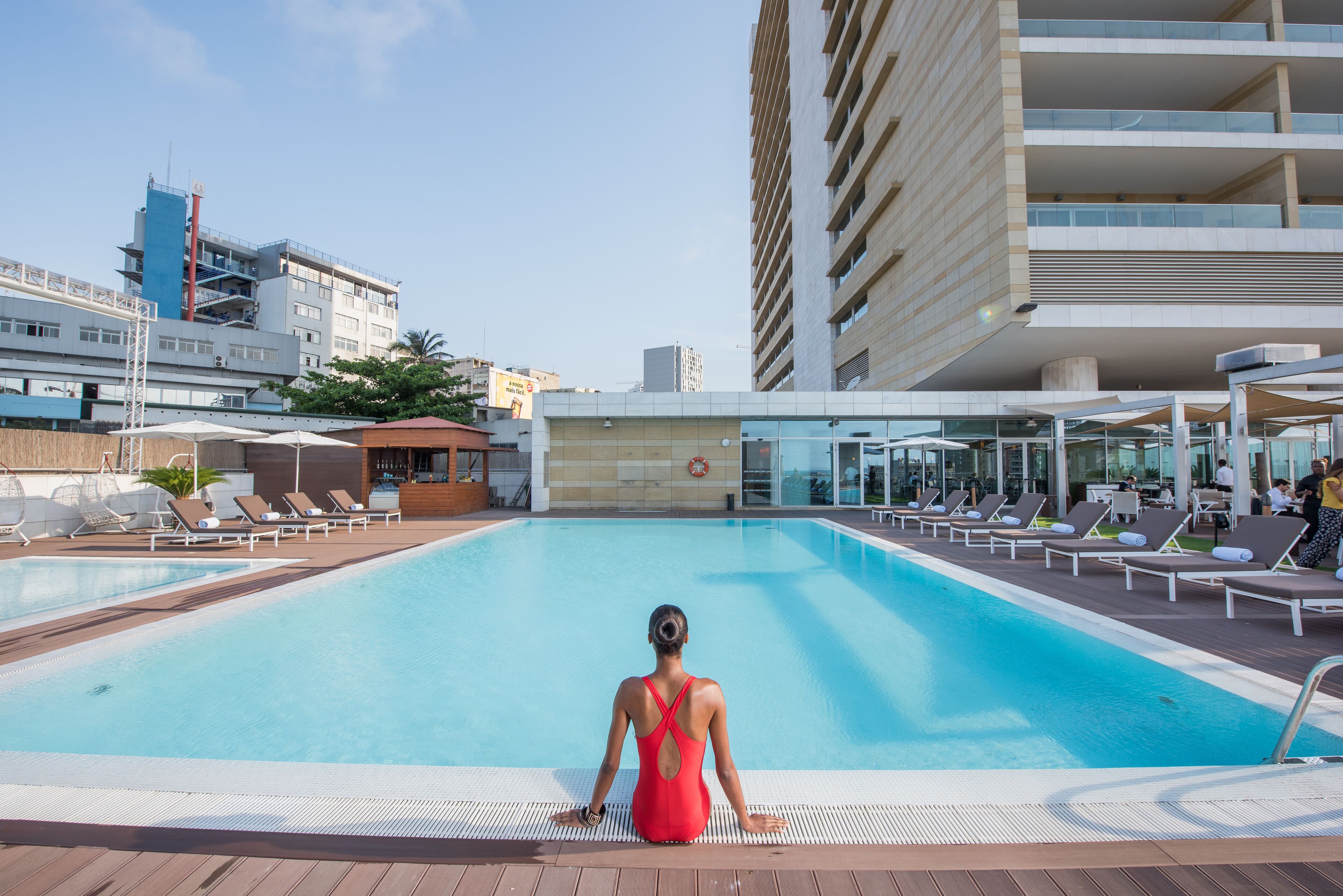 Área da piscina com espreguiçadeiras e uma mulher de fato de banho vermelho.