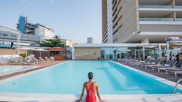 Área da piscina com espreguiçadeiras e uma mulher de fato de banho vermelho.
