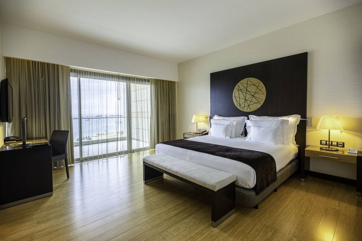 A modern hotel room with a large bed, a bench, a desk, and a TV.