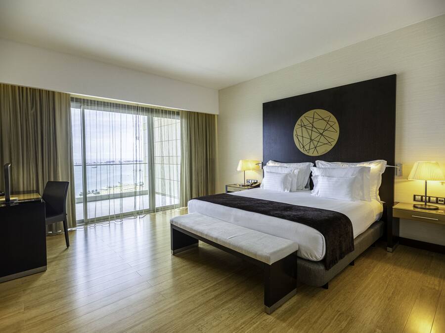 A modern hotel room with a large bed, a bench, a desk, and a TV.