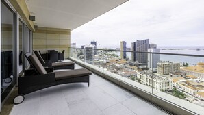 A balcony with two lounge chairs, a glass wall, and a city view. - EPIC SANA Luanda Hotel (Luanda)