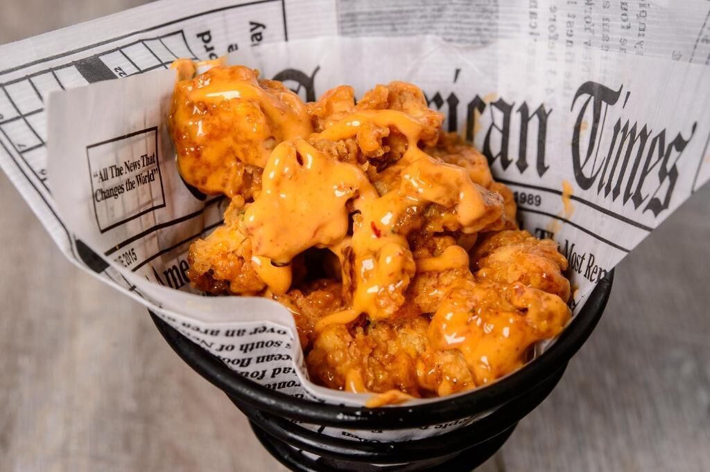 A bowl of fried chicken with sauce, placed on a newspaper.