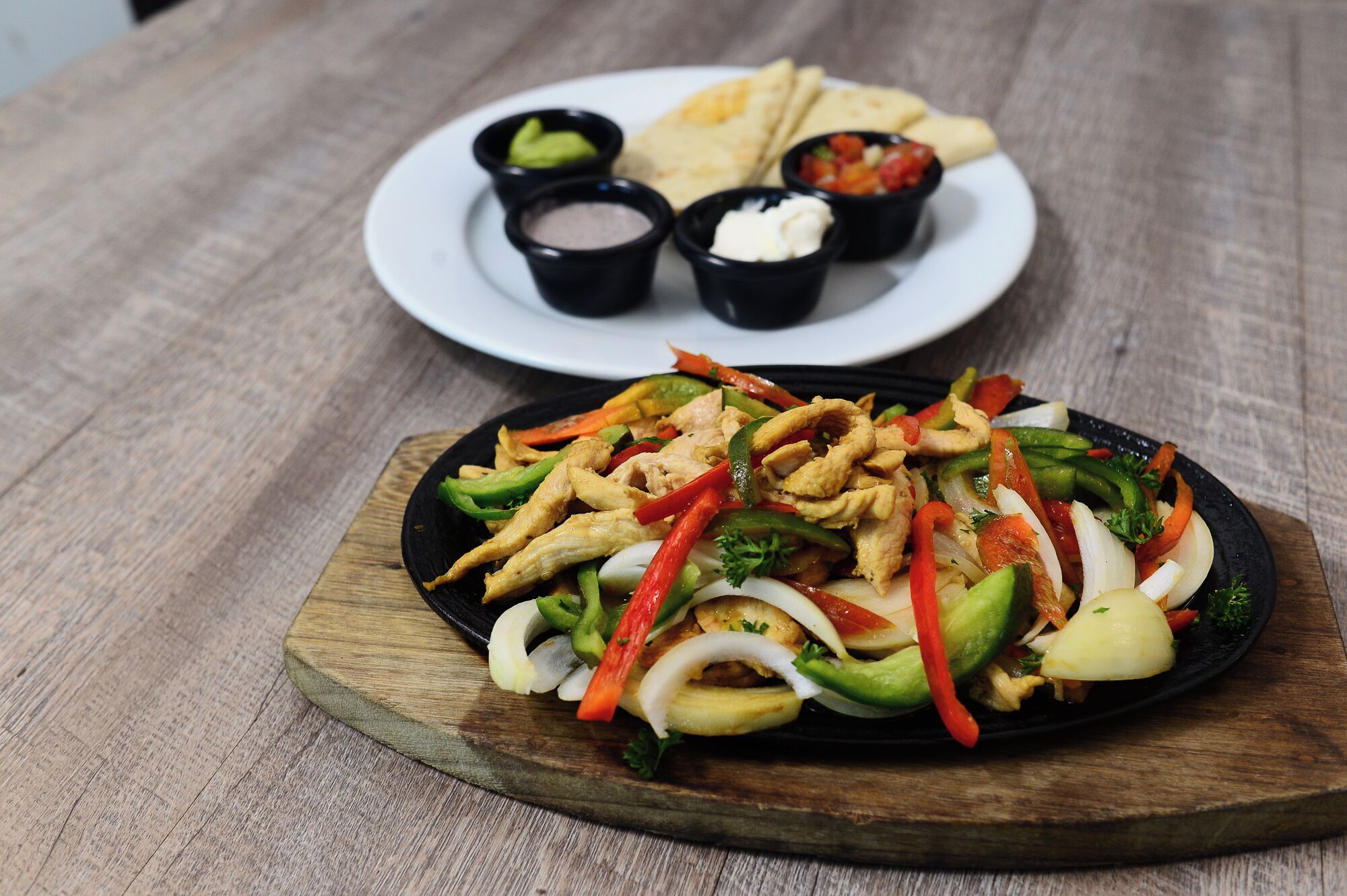 Un tavolo di legno con un piatto di fajitas e un piatto di flatbread e salse.