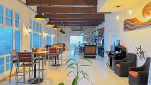 Ein großzügiges Café mit hohen Decken, großen Fenstern und verschiedenen Sitzgelegenheiten, darunter Tische und Stühle.