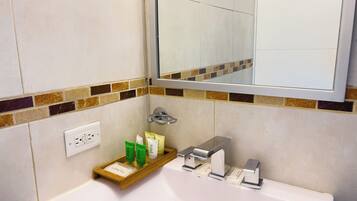 Un baño con un lavabo blanco, un espejo encima y un estante con artículos de aseo.