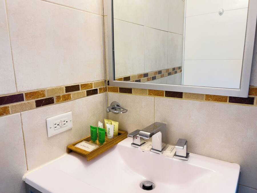 Un baño con un lavabo blanco, un espejo encima y un estante con artículos de aseo.
