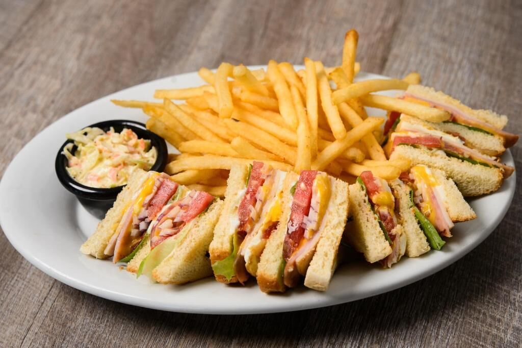 Un plato con un sándwich cortado en triángulos, una porción de papas fritas y un tazón pequeño de ensalada de col.