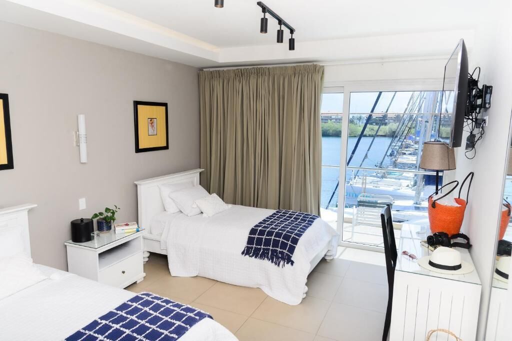 A hotel room with a bed, a desk, a chair, a window with a view of a body of water, and a television mounted on the wall.