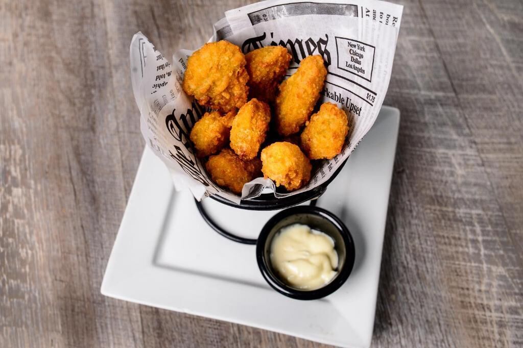 A basket of fried food items on a white plate with a small bowl of sauce.