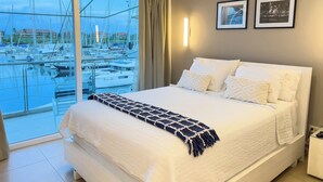 Ein Hotelzimmer mit einem großen Bett, Blick auf einen Jachthafen und zwei gerahmten Bildern an der Wand.