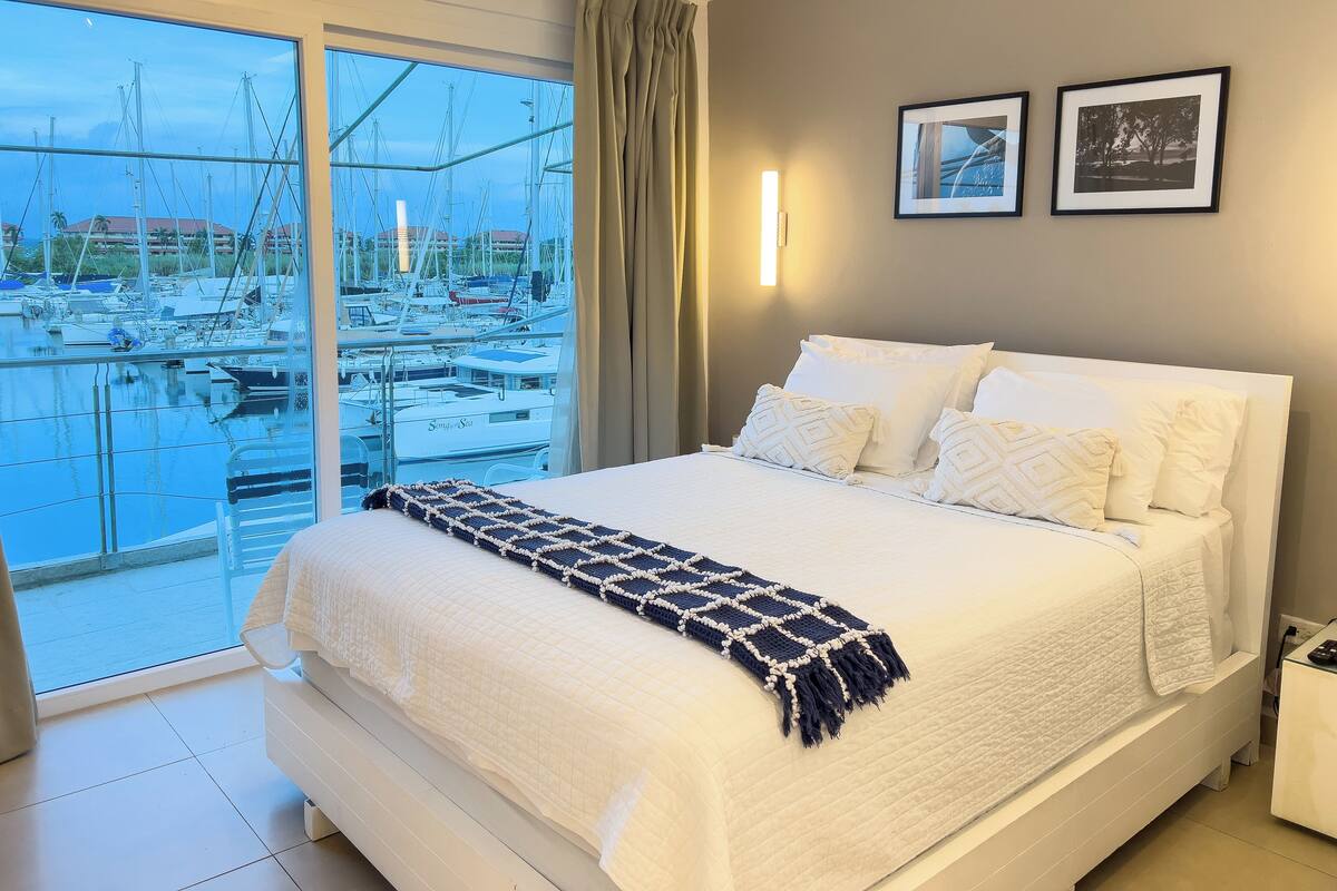 A hotel room with a large bed, a view of a marina, and two framed pictures on the wall.