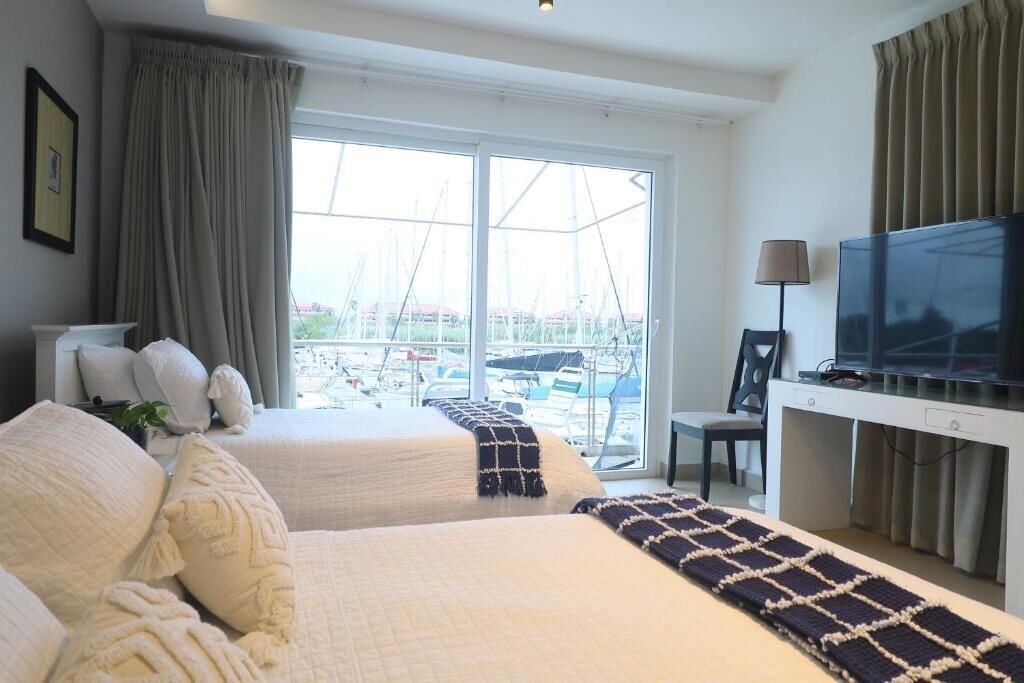 Habitación de hotel con dos camas, televisión y vista al puerto deportivo.