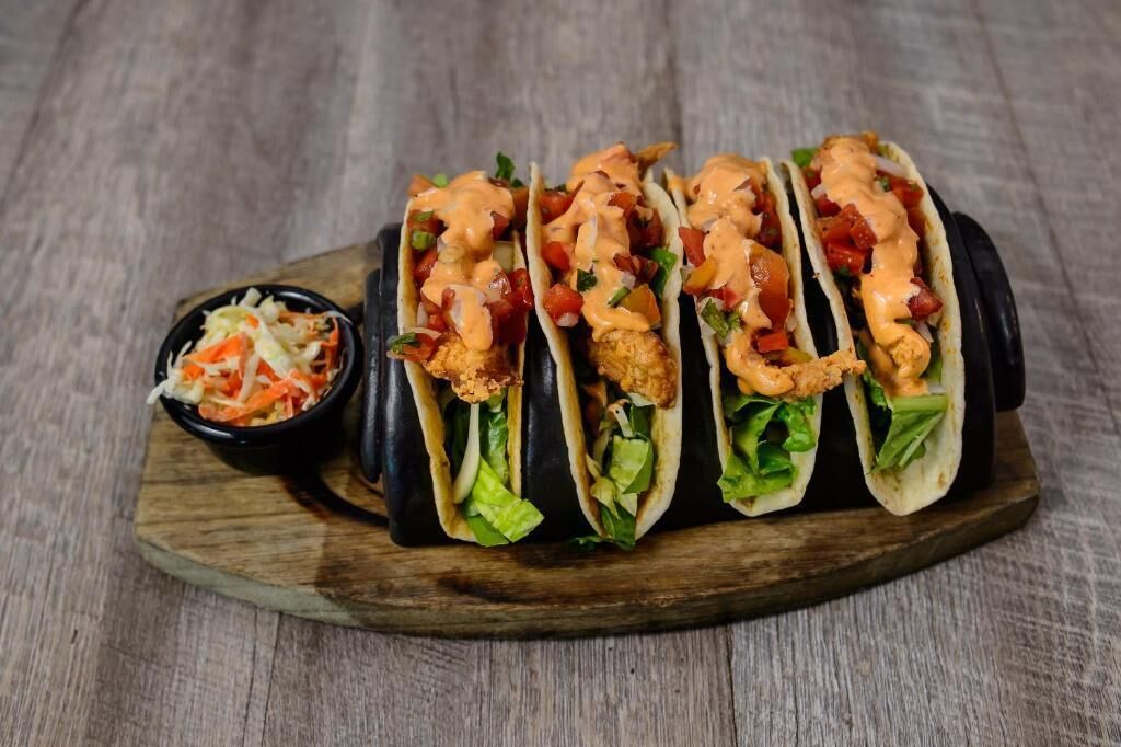 Uma tábua de madeira com quatro tacos e uma pequena tigela de salada de repolho.