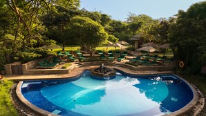 A circular pool with a waterfall feature surrounded by green lounge chairs and umbrellas.