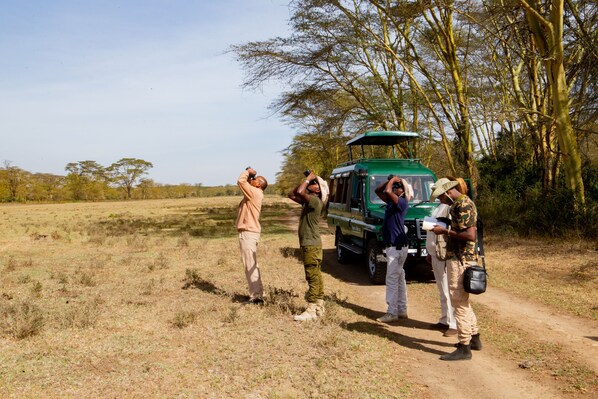 A safari vehicle parked on a dirt path with people standing beside it.