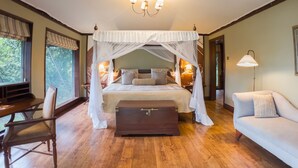 A bedroom with a four-poster bed, a wooden chest of drawers, a sofa, and a desk with a chair.