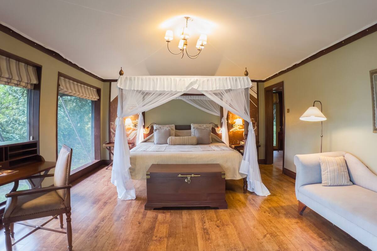 Une chambre à coucher avec un lit à baldaquin, une commode en bois, un canapé et un bureau avec une chaise.