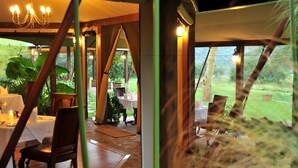 An indoor dining area with tables set for a meal, wooden chairs, and a view of the outdoors.