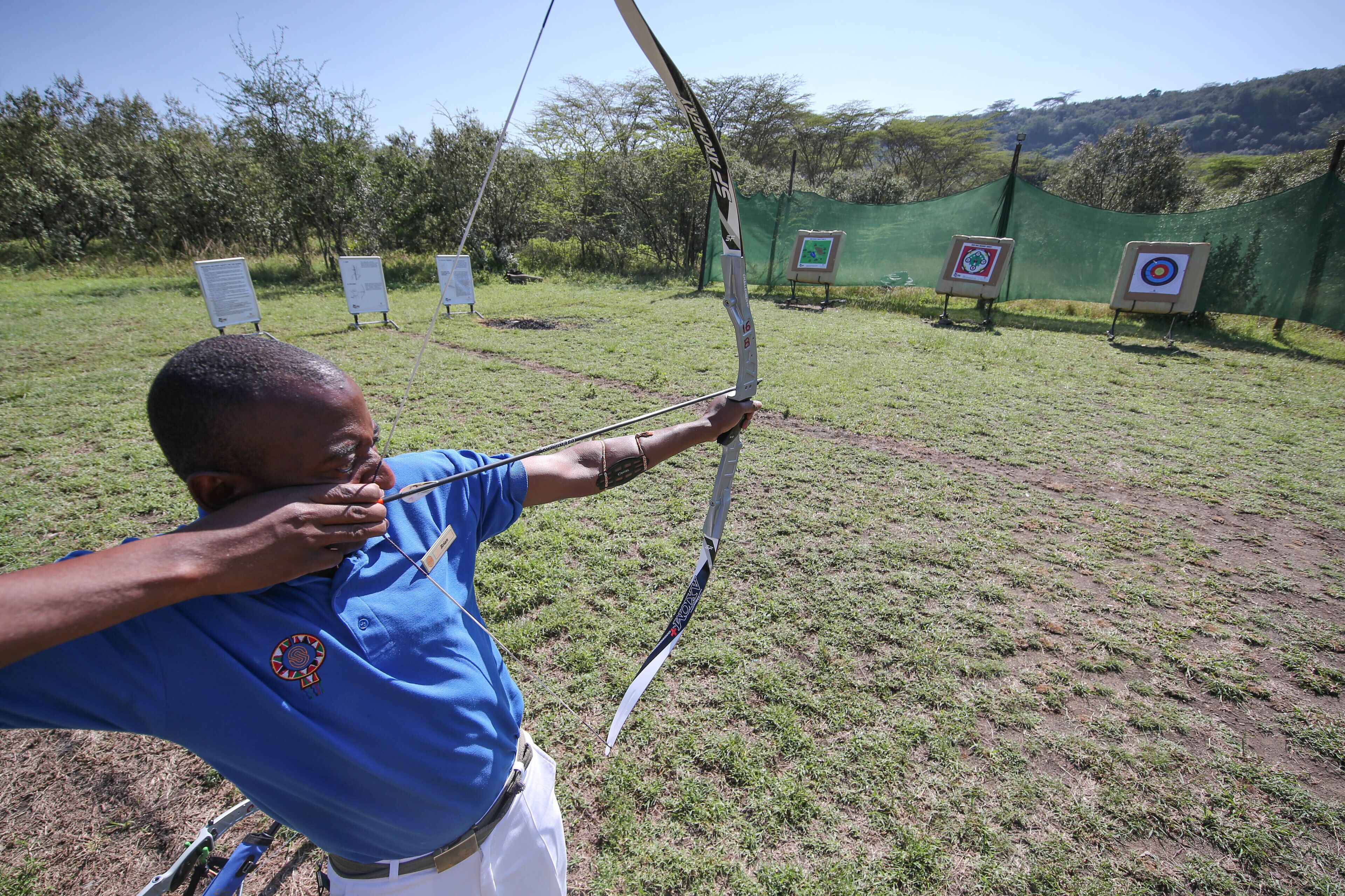 An outdoor archery range with targets and a person in blue attire aiming a bow.