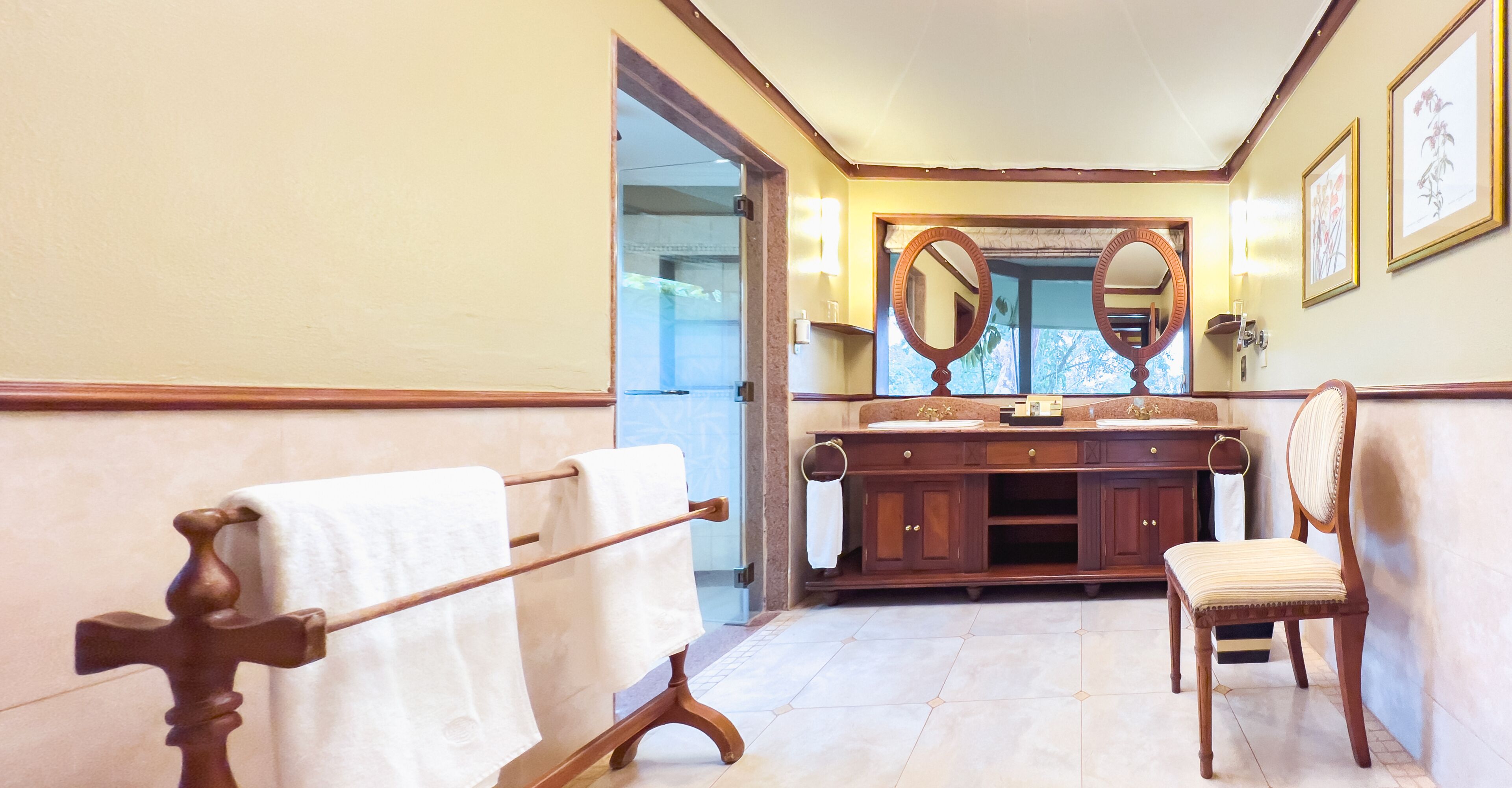A bathroom with a wooden vanity, a large mirror, a towel rack, and a chair.