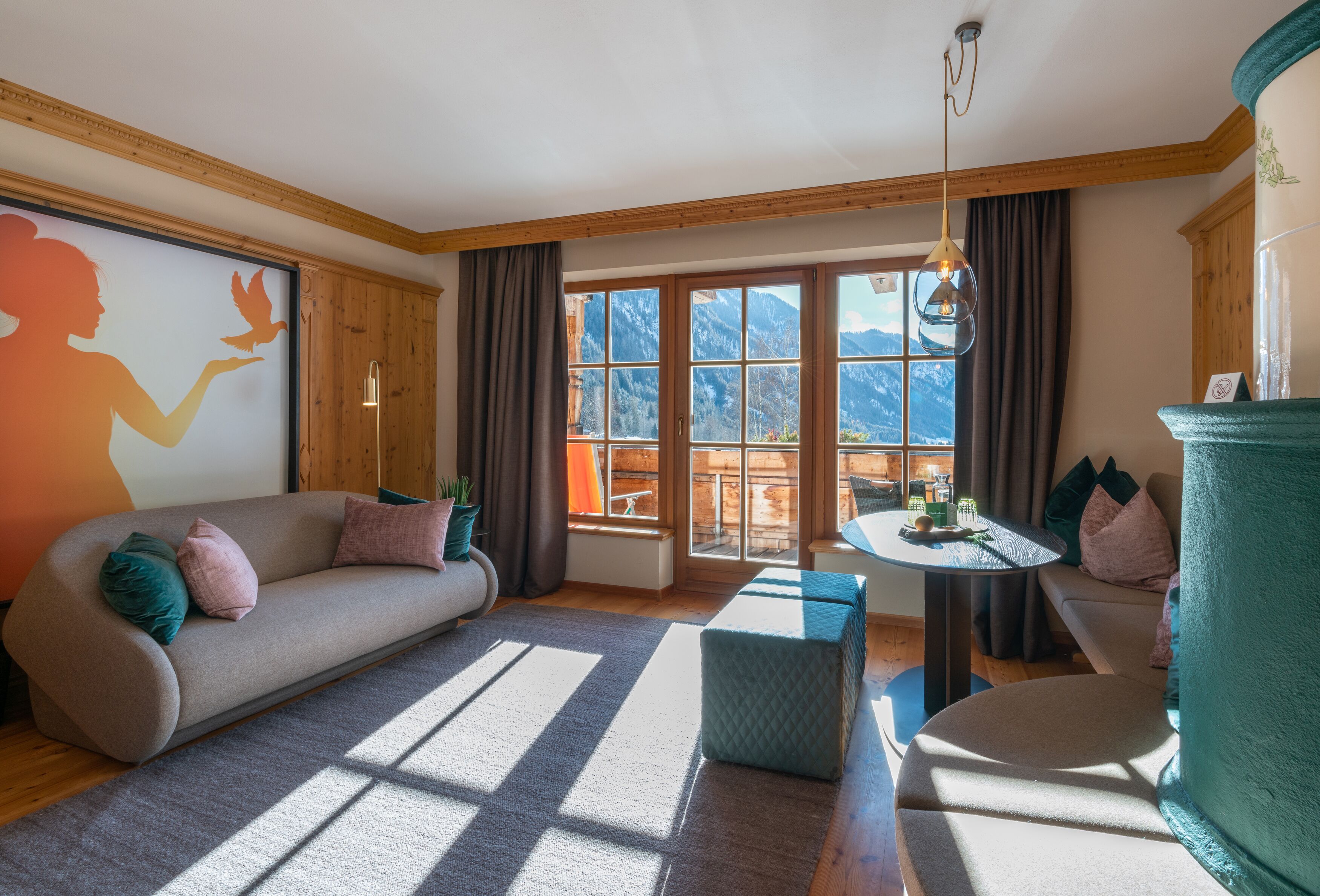Una sala de estar moderna con sofá, reposapiés y una mesita. Amplias ventanas ofrecen vistas a las montañas.