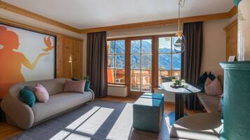 Una sala de estar moderna con sofá, reposapiés y una mesita. Amplias ventanas ofrecen vistas a las montañas.