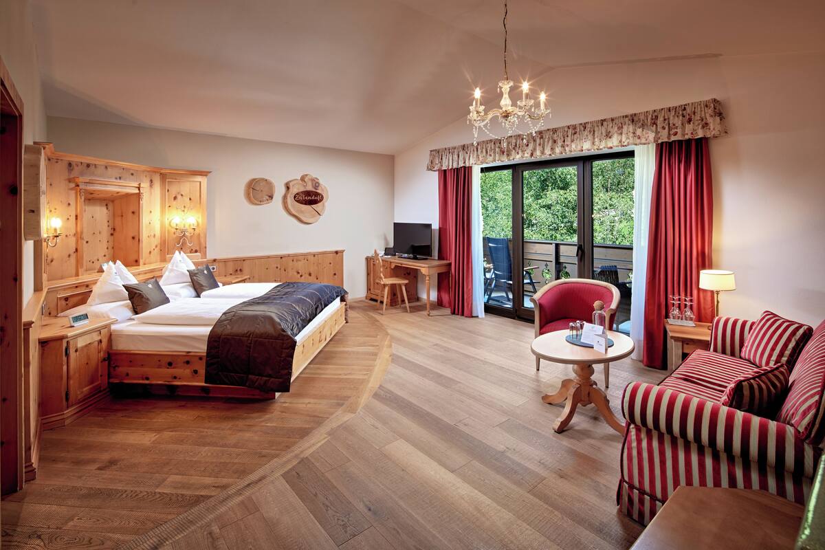 Ein holzmöbliertes Zimmer mit einem Bett, einem Schreibtisch, einem Sessel und einem Sofa.
