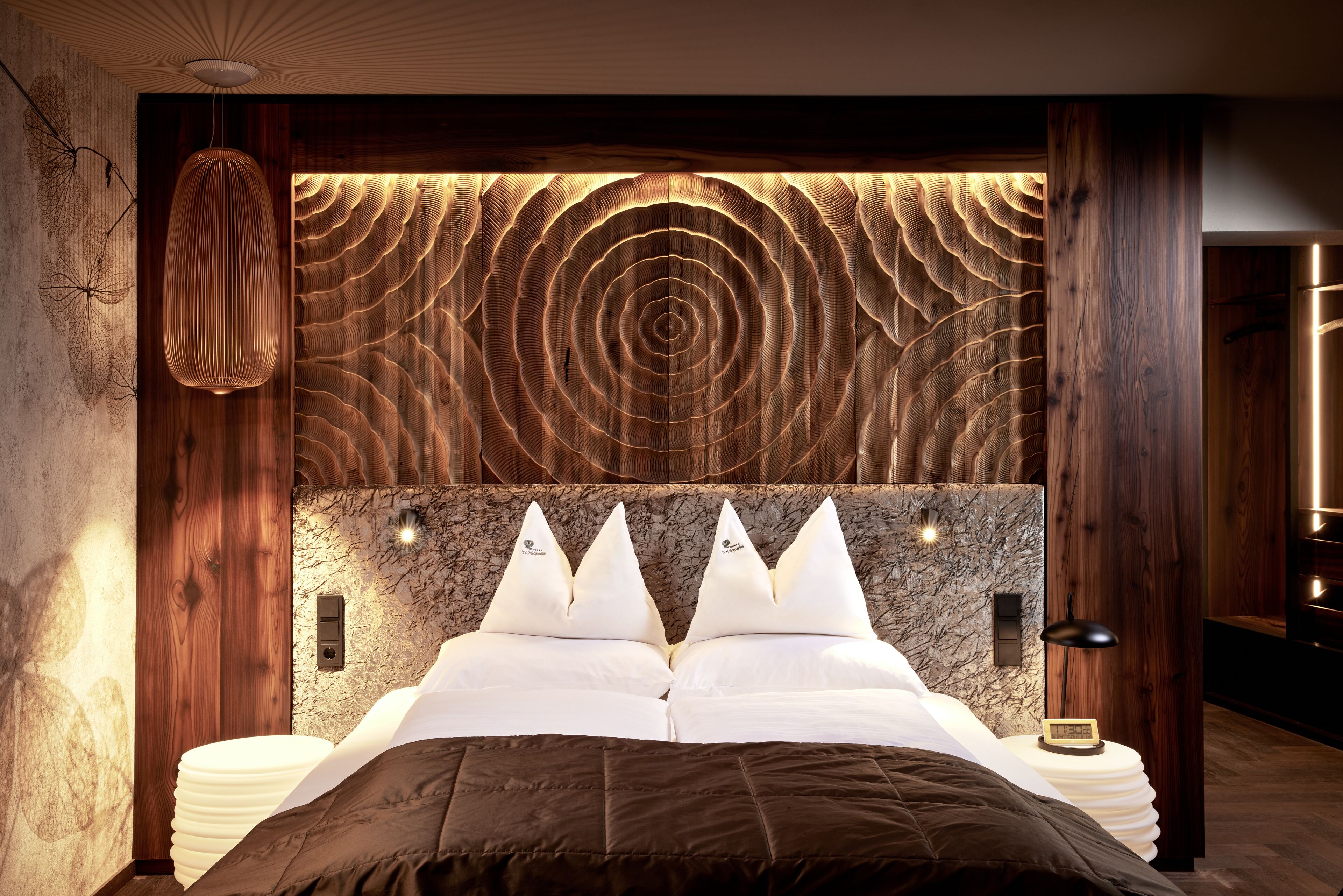 Un dormitorio moderno con cabecera de madera, pared con diseño de mármol y cama con ropa de cama blanca.