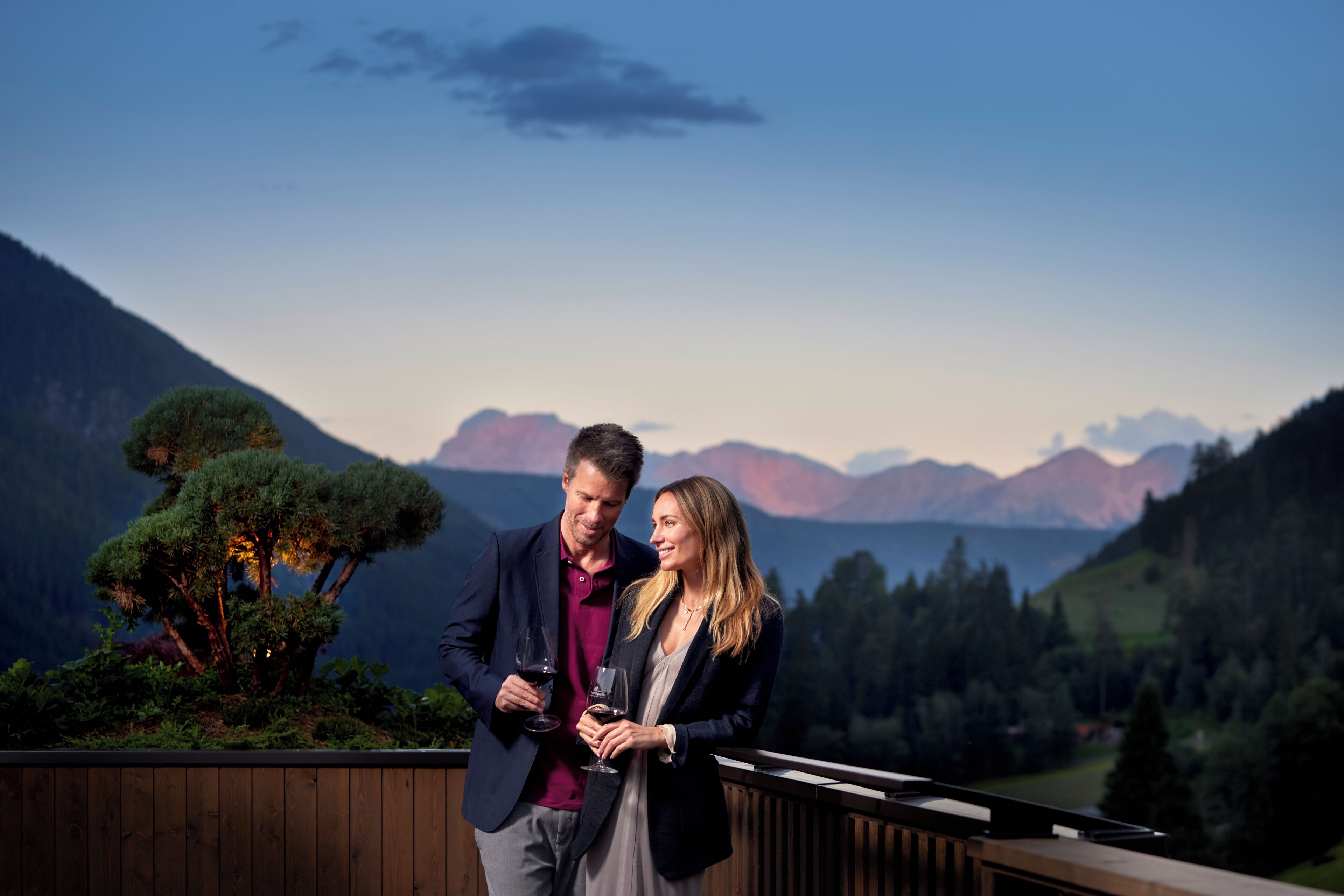 A couple standing on a balcony overlooking a mountainous landscape.
