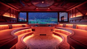 A wooden interior with a large TV screen, curved seating, and a stone floor. - Hotel Quelle Nature Spa Resort (Valle di Casies)
