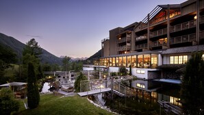 A multi-story hotel with a pool, outdoor seating, and mountain views. - Hotel Quelle Nature Spa Resort (Valle di Casies)