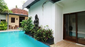 A swimming pool with a statue, potted plants, and a door with a glass panel. - Alam Bali Hotel (Nusa Dua)