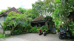 A paved driveway with two motorcycles parked, surrounded by lush greenery and a building with a tiled roof. - Alam Bali Hotel (Nusa Dua)