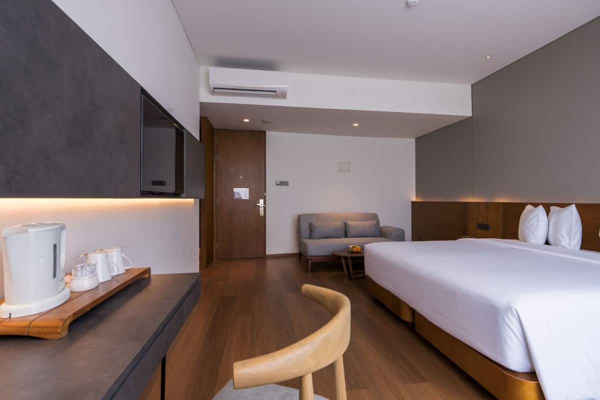 Una habitación de hotel moderna con una cama grande, un escritorio con cafetera, un sofá y un televisor montado en la pared.