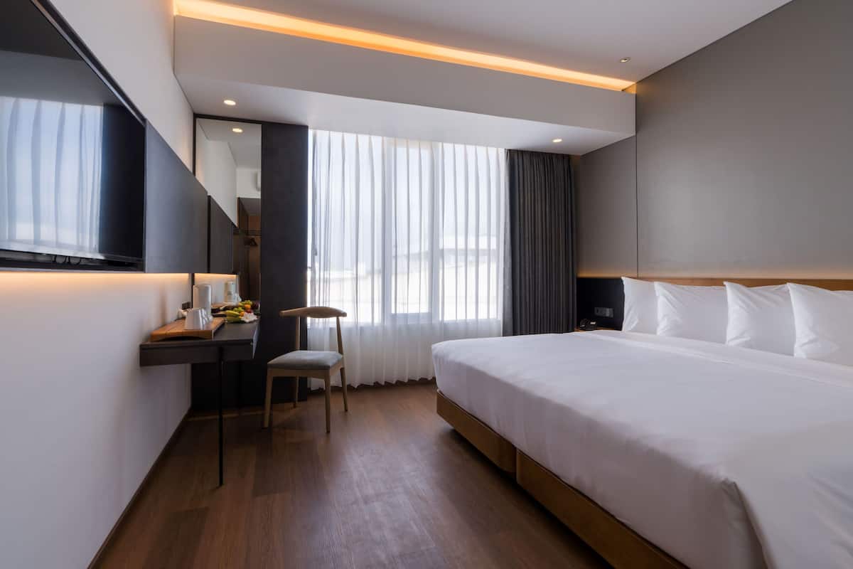 Una habitación de hotel moderna con una cama grande, un escritorio con silla, un televisor de pantalla plana y un ventanal con cortinas.