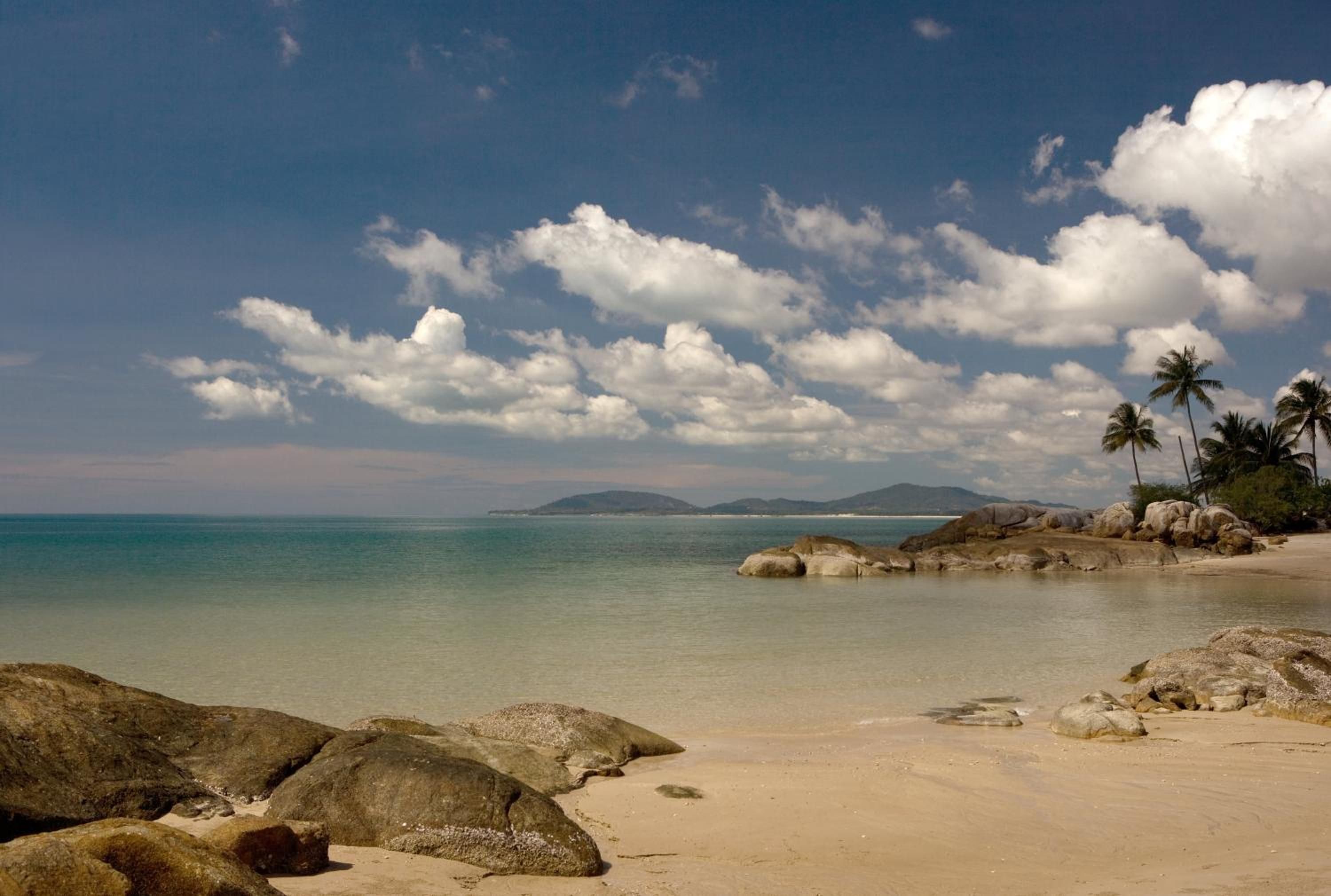Ein Strand mit blauem Himmel, ruhigem Wasser und Felsen.