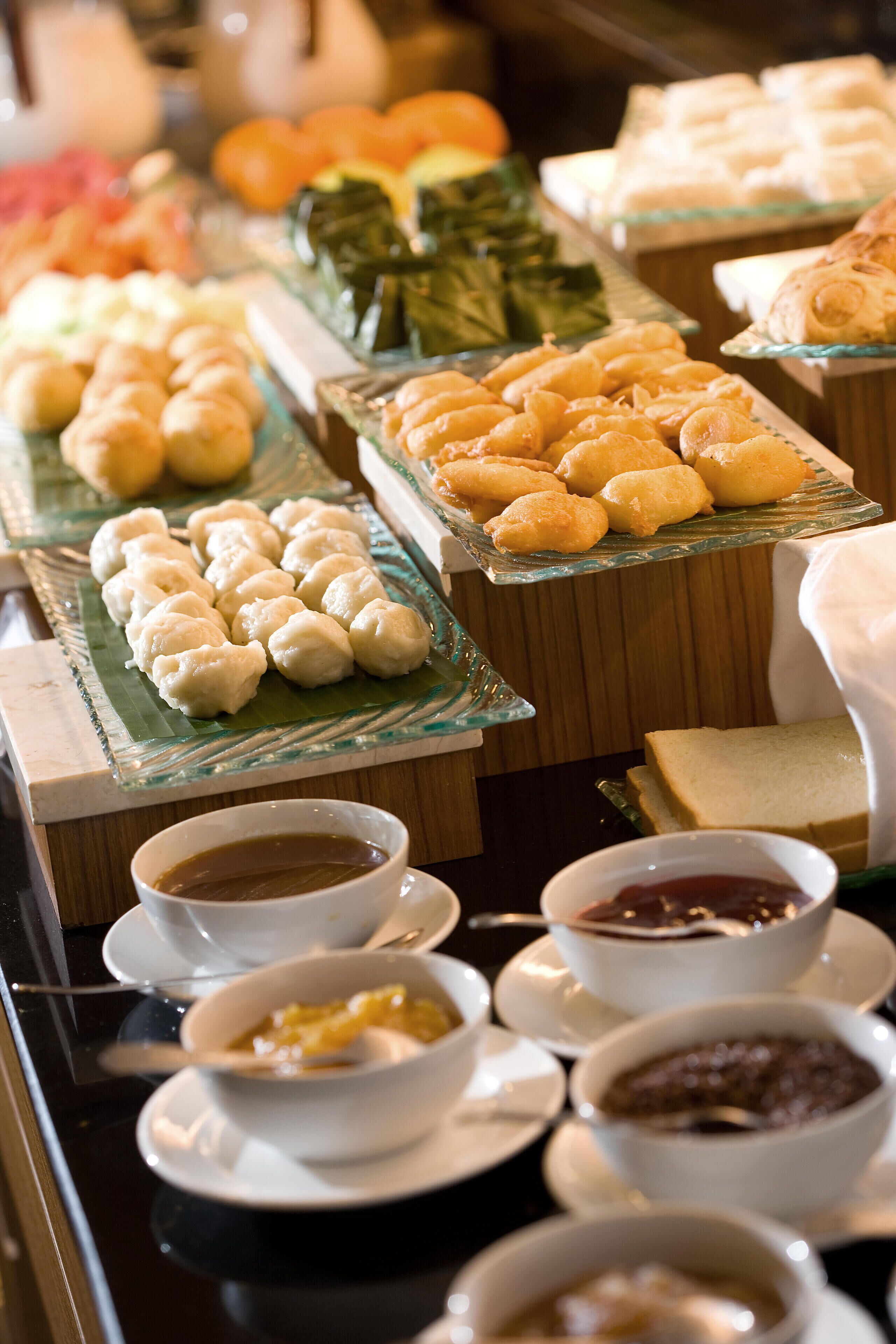 A buffet with various food items including pastries, fruits, and bowls of soup.